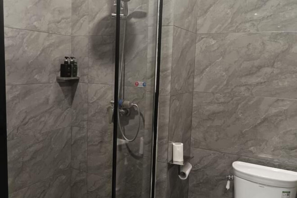 A bathroom with a glass shower enclosure, a toilet, and a shelf with toiletries.