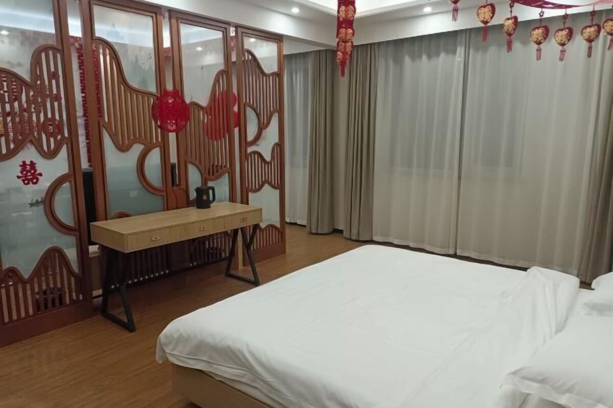 A hotel room with a bed, a wooden desk, and a traditional Chinese-style partition.
