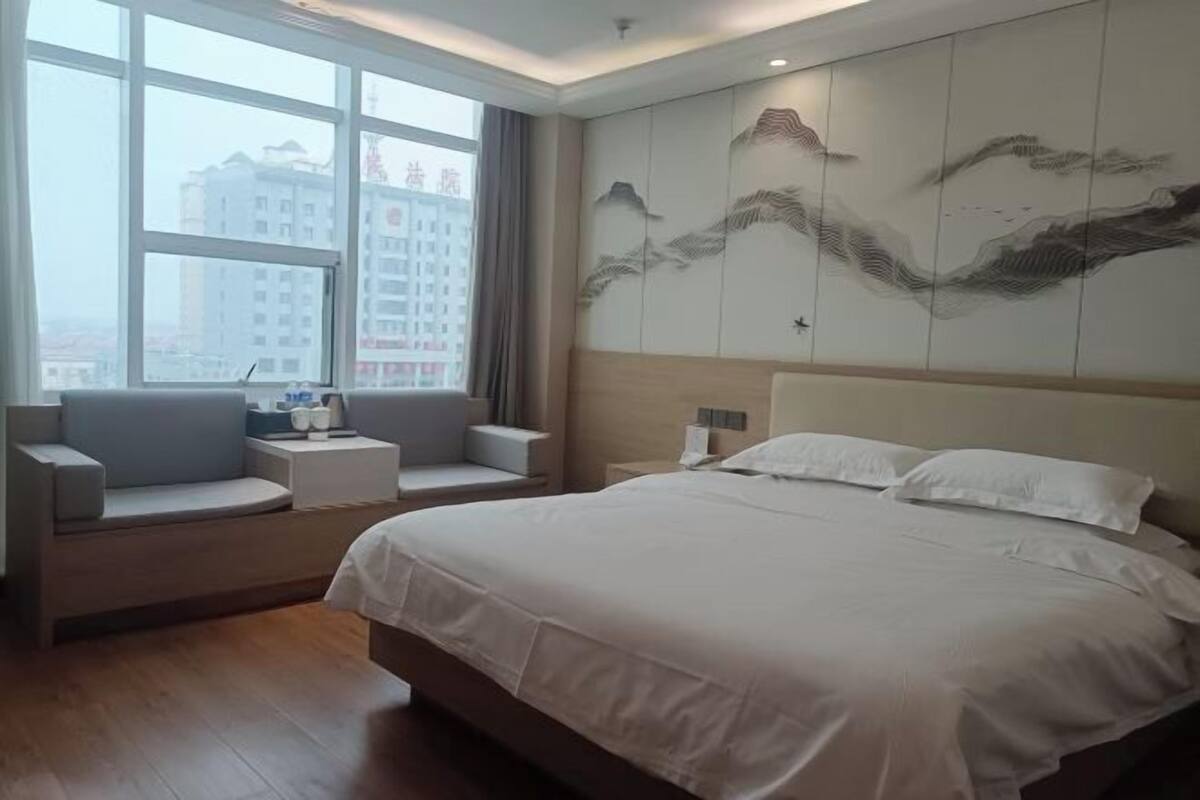 A hotel room with a large bed, a seating area with a view, and a wall with artwork.