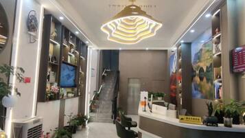 A hotel lobby with a reception desk, a staircase, and a modern chandelier.