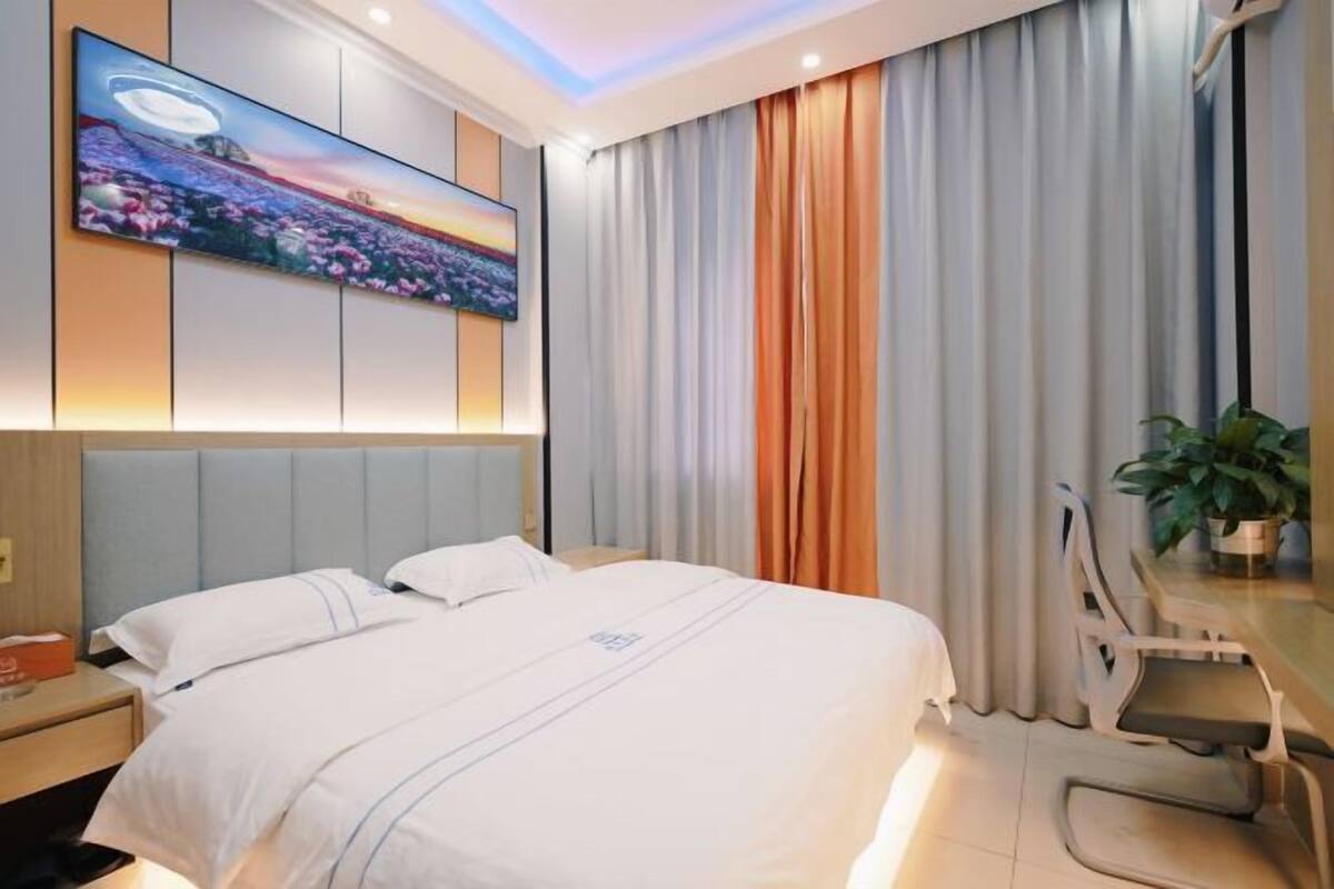 Ein Hotelzimmer mit einem Bett, einem Schreibtisch mit Stuhl, einem flachbildfernseher an der Wand und einem Fenster mit Vorhängen.