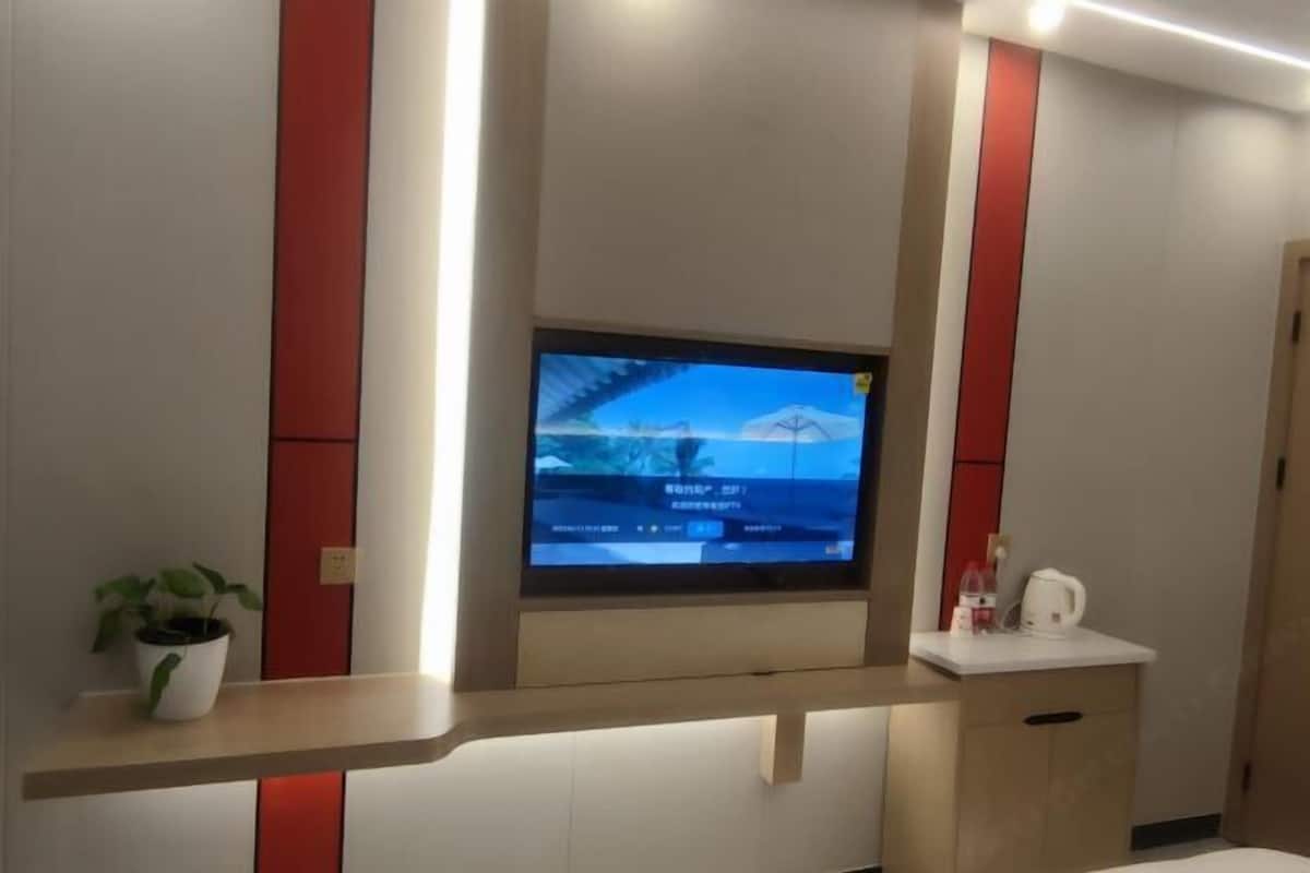 Ein an der Wand befestigter Fernseher mit rotem Akzent, ein Blumentopf und ein kleiner Tisch mit einem Wasserkocher.