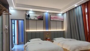 Ein Hotelzimmer mit zwei Betten, einem Flachbildfernseher, einer Minibar und einem großen Fenster mit Vorhängen.