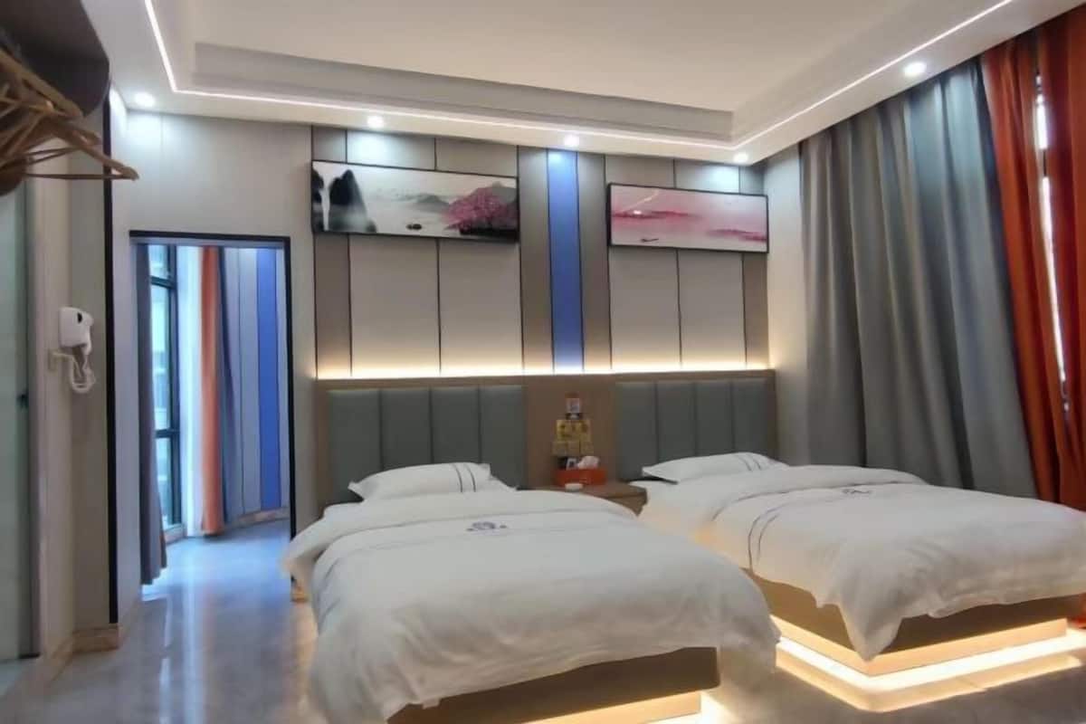 Ein Hotelzimmer mit zwei Betten, einem Flachbildfernseher, einer Minibar und einem großen Fenster mit Vorhängen.