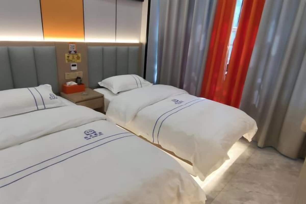 Ein Hotelzimmer mit zwei Betten, einem Nachttisch, einer wandmontierten Steuerung und einem Fenster mit Vorhängen.