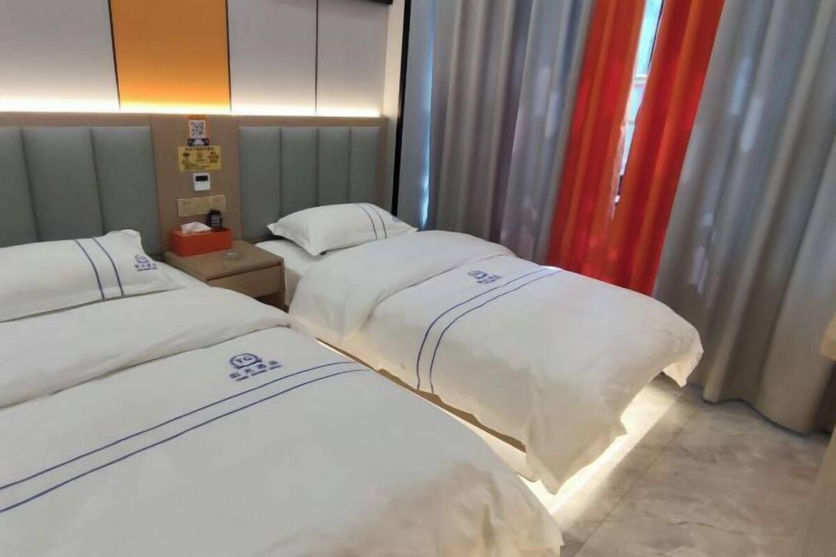 Ein Hotelzimmer mit zwei Betten, einem Nachttisch, einem an der Wand montierten Fernseher und einem Fenster mit Vorhängen.