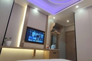 Une chambre d’hôtel avec un lit, un téléviseur fixé au mur diffusant une visioconférence, une plante en pot et un miroir.