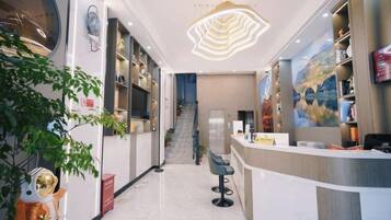 A hotel lobby with a reception desk, a staircase, and a large painting on the wall.