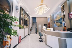 Un hall d’hôtel avec un comptoir d’accueil, un escalier et un grand tableau accroché au mur.