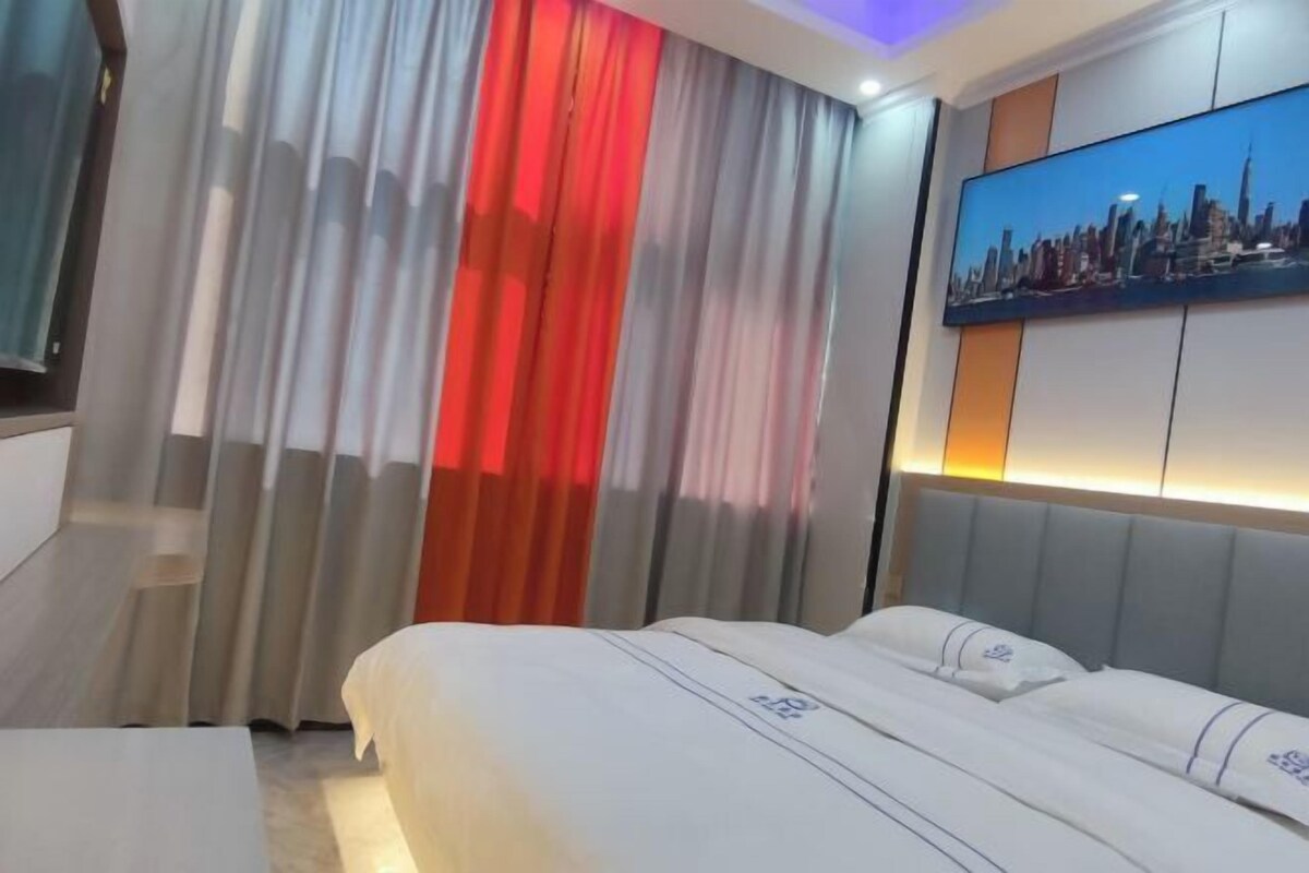 Une chambre d’hôtel avec un lit, des rideaux, un tableau représentant un paysage urbain et un escalier.