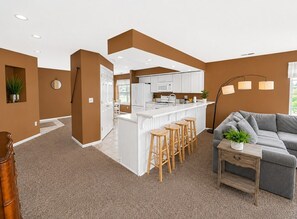 A modern kitchen with white cabinets, a bar area with stools, and a grey sofa in a living area with brown walls and a brown carpet. - Lounging on the Links (Branson)