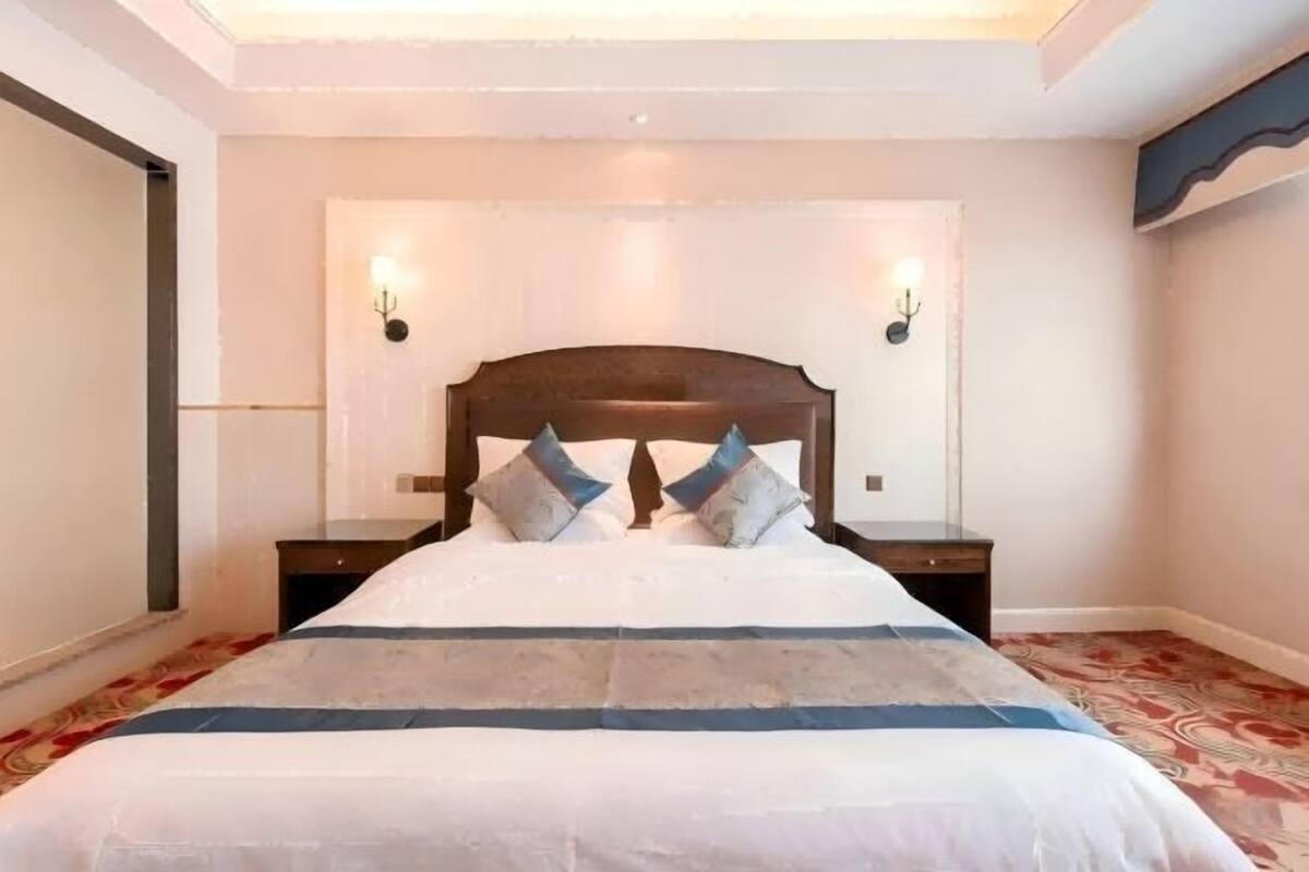 A bedroom with a large bed, two bedside tables, and wall-mounted lights.