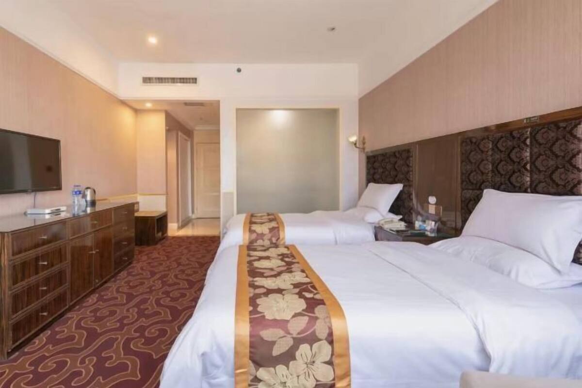A hotel room with two beds, a TV, a minibar, and a patterned carpet.