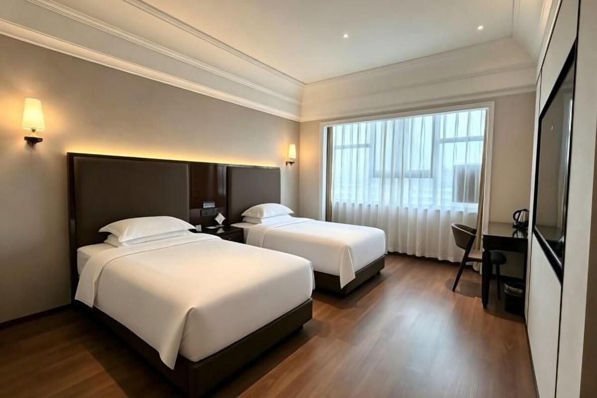 A hotel room with two beds, a desk, and a chair.