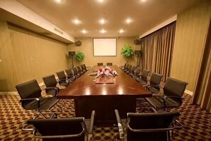 Un salón de conferencias con una larga mesa, sillas, una pantalla de proyector y plantas.