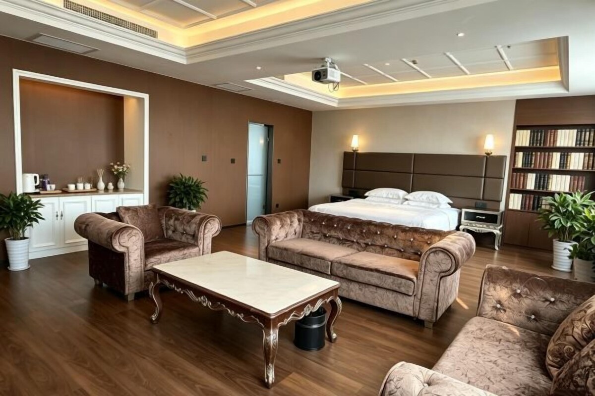 A hotel room with a large bed, two sofas, a coffee table, a desk, and a bookshelf.