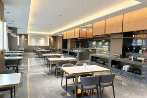 Un restaurant moderne doté d’un long comptoir, de plusieurs espaces de restauration et d’une cuisine visible au fond de la salle.