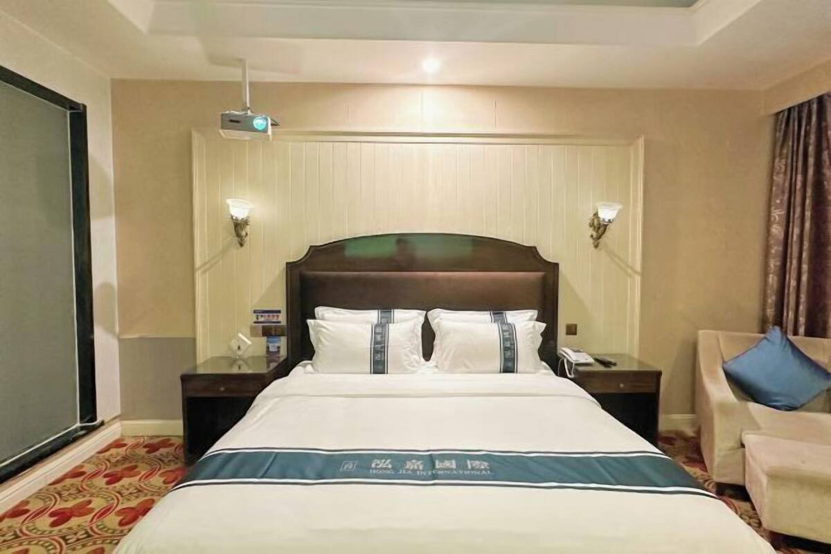 A hotel room with a large bed, two bedside tables, a chair, a television, and a projector mounted on the ceiling.