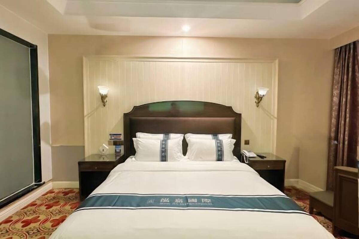 A hotel room with a large bed, two bedside tables, a nightstand, and a wall-mounted lamp.