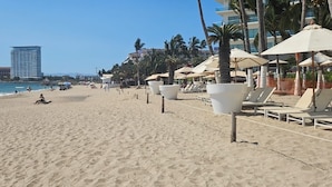 Una playa con tumbonas y sombrillas, un cielo despejado y un edificio alto al fondo.