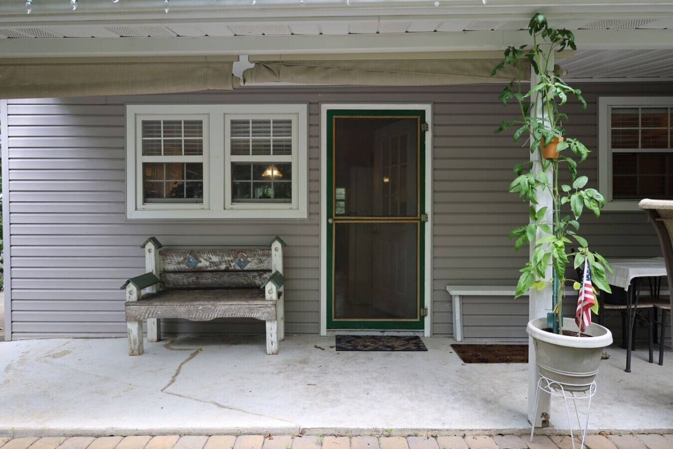 A porch with a bench, a potted plant, and a door.