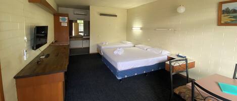 Habitación de hotel con cama, escritorio, silla, televisor y baño visible a través de una puerta abierta.