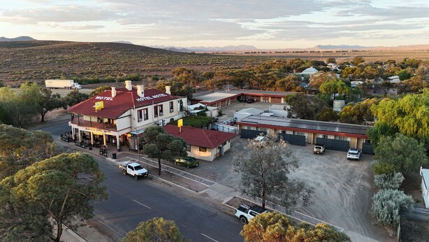 A motel with a red roof, a parking lot, and a view of the surrounding landscape. - Hawker Hotel Motel (Hawker)