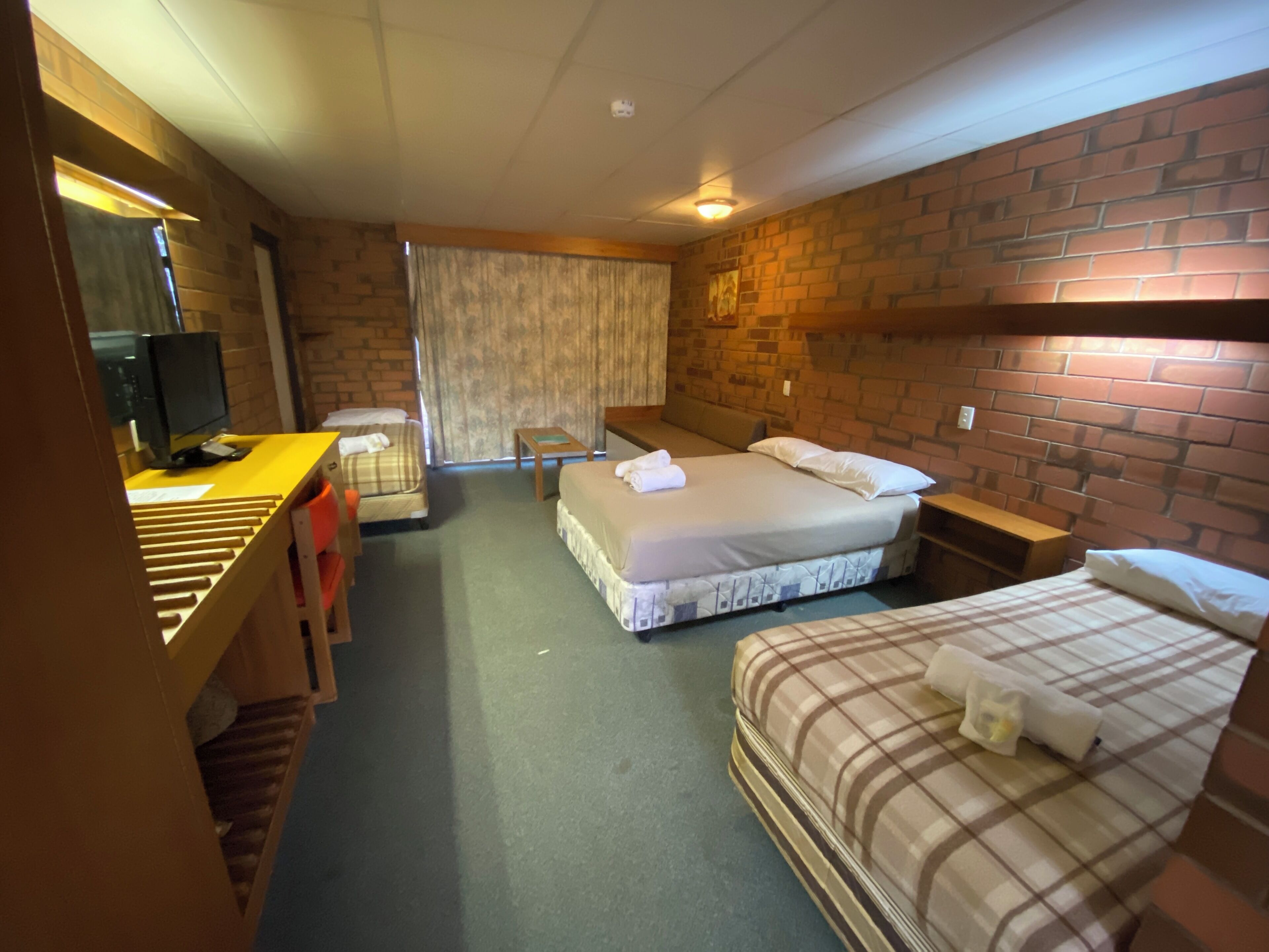 A hotel room with two beds, a desk, a chair, a television, and a window with curtains.