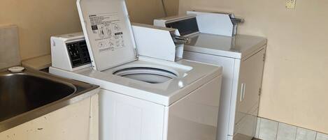 Een wasruimte met een wasmachine en droger, een wastafel, en een bordje met de gesloten tijden van de gastenwasserij.
