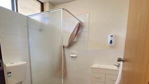 A bathroom with a toilet, a glass shower enclosure, a sink, and a soap dispenser. - Hawker Hotel Motel (Hawker)