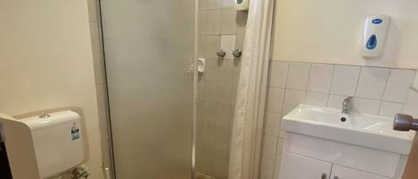 A bathroom with a toilet, a shower enclosure, a sink, and a soap dispenser.