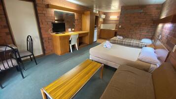 A compact room with a bed, a desk, a chair, a television, and a small kitchenette.