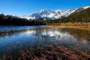 A clear lake with reflections, a mountain range, and a forested area. - Xiyi Shengshi Hotel (Luding)