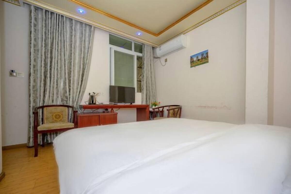 Ein Hotelzimmer mit Bett, Schreibtisch, Stuhl, einem Fenster mit Vorhängen und einer Klimaanlage.