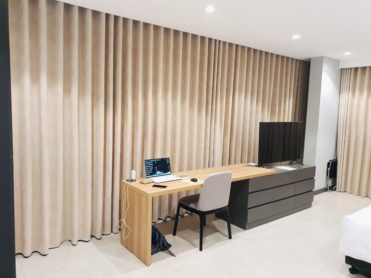 Une chambre d’hôtel avec un bureau en bois, une chaise, une télévision, un lit et une grande fenêtre avec des rideaux.