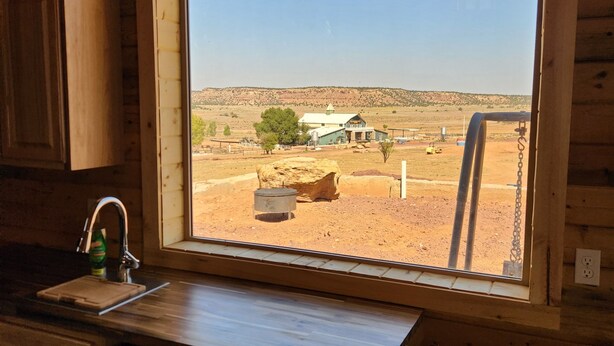 A wooden cabin interior with a large window overlooking a desert landscape, a sink, and a chair. - The Rocky Mountain Cabin (Hurricane)