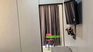 A room with a bed, a table, a TV mounted on the wall, and a curtain-covered window. - Debao Hongshanyuan Hotel (Debao)