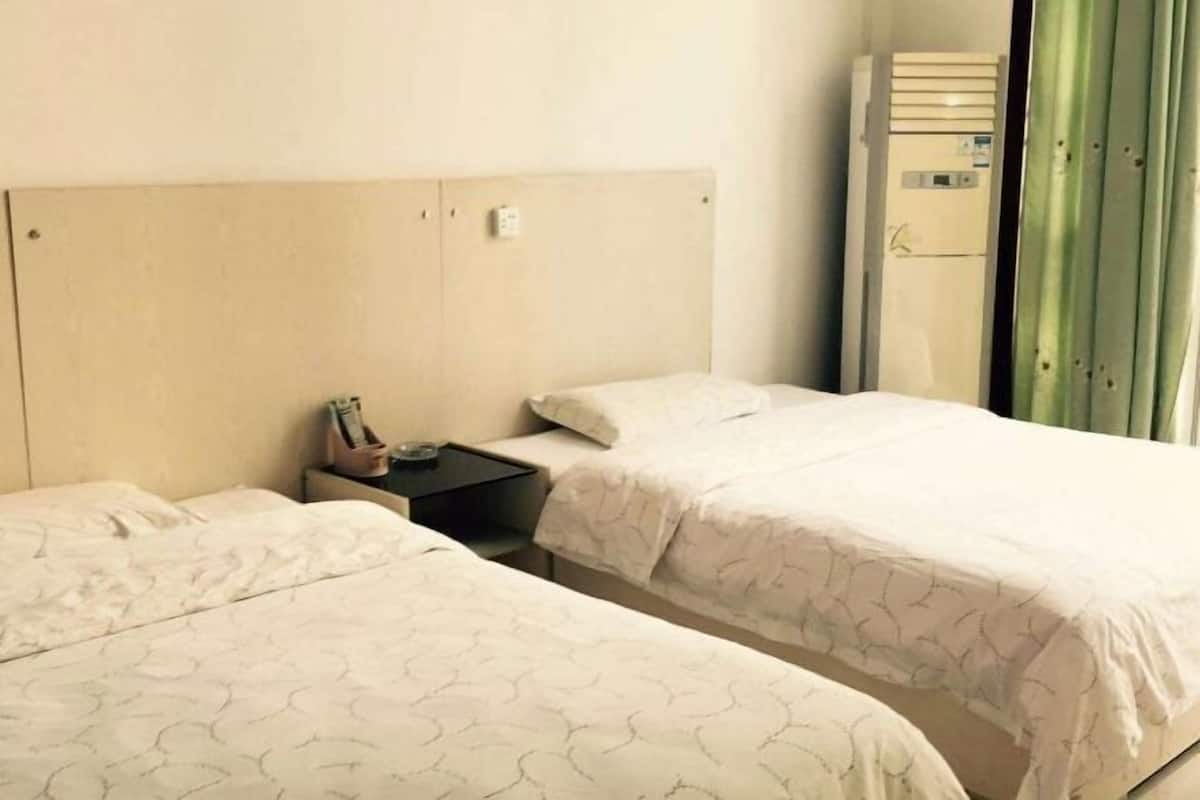 A hotel room with two beds, a nightstand, a small table, and a window with curtains.