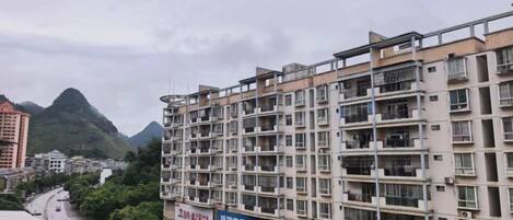 A multi-story residential building with balconies, a clear sky, and a mountain in the background.