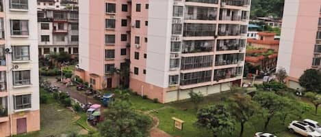 A high-rise residential building with multiple balconies, a central courtyard, and a parking area.