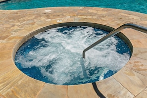 A hot tub with a metal ladder, surrounded by a stone pool area.
