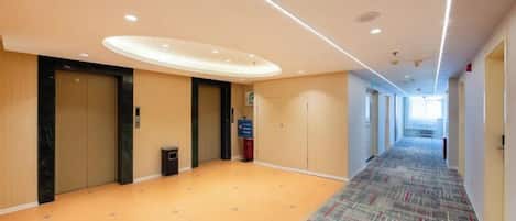 Un pasillo de hotel con suelo alfombrado, iluminación empotrada y puertas que dan a las habitaciones.