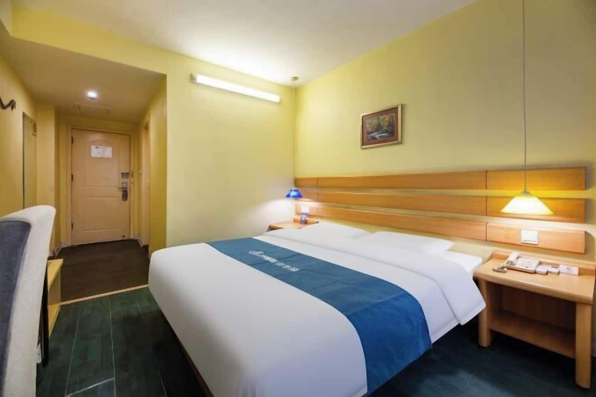 Ein Hotelzimmer mit Bett, Nachttisch, Lampe und einer Tür zu einem Flur.