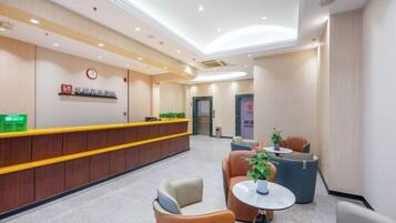 Zona de recepción de un hotel con mostrador, área de descanso y una puerta al fondo.