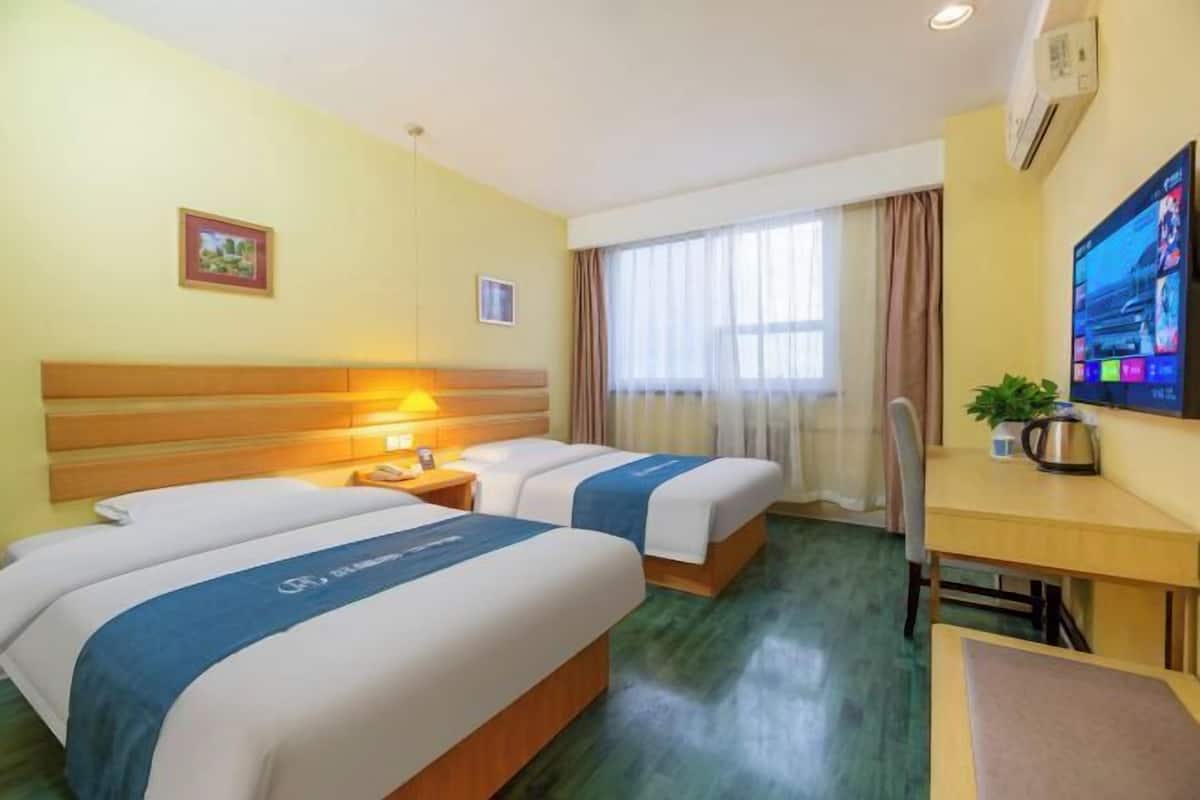 Ein Hotelzimmer mit zwei Betten, einem Schreibtisch, einem Stuhl, einem Fernseher und einem Fenster mit Vorhängen.