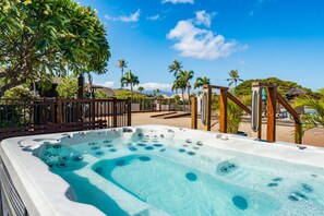 Een hottub met een zwembad in helderblauw, omgeven door een houten hek, palmbomen en een heldere lucht.