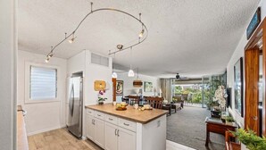 A modern kitchen with a central island, white cabinetry, and a stainless steel refrigerator. - West Maui 1BR condo with lanai, pool, AC, beach access & resort views.- EL E204 (Lahaina)