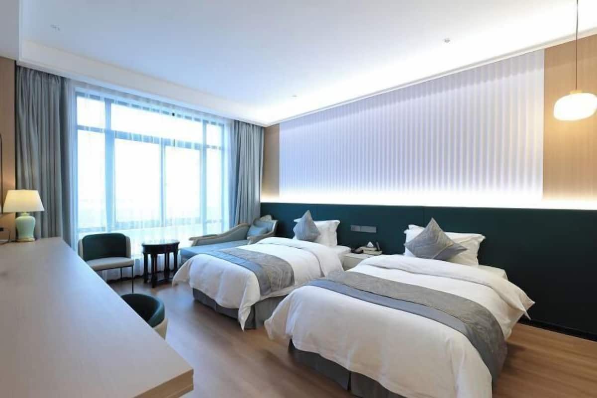 A hotel room with two beds, a desk, a chair, and a large window with curtains.