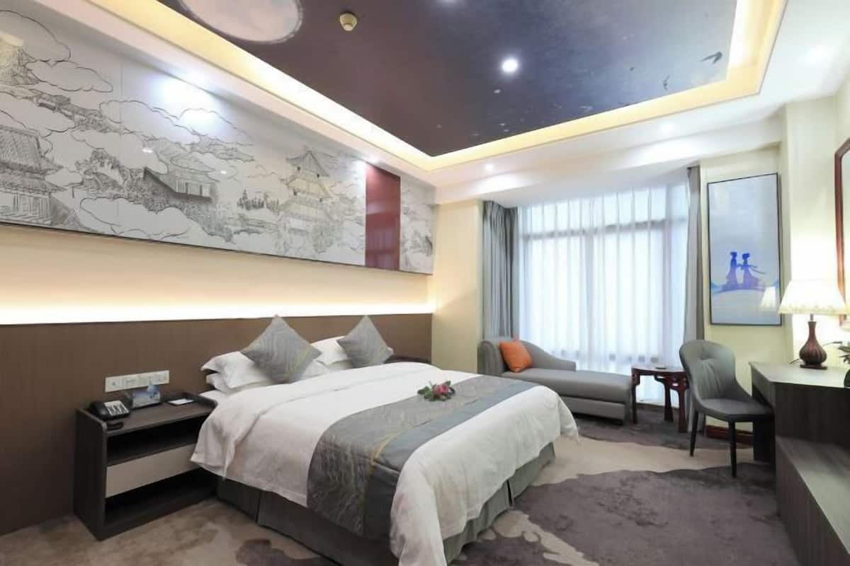 A hotel room with a bed, bedside table, lamp, chair, and a large wall mural.