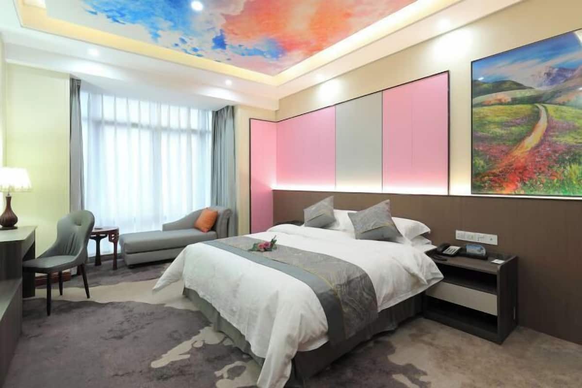 A hotel room with a large bed, a desk, a chair, a nightstand, and a painting on the wall.